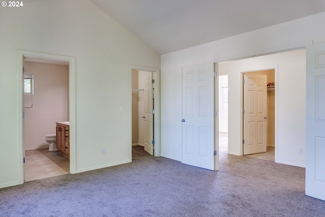 unfurnished bedroom featuring a spacious closet, vaulted ceiling, light colored carpet, and a closet