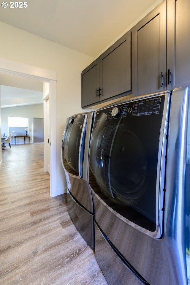 washroom with baseboards, cabinet space, light wood-style floors, and washing machine and clothes dryer