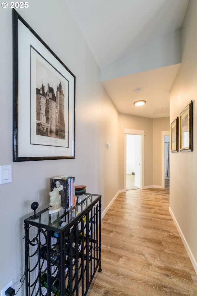 hall with vaulted ceiling, light wood-style flooring, and baseboards