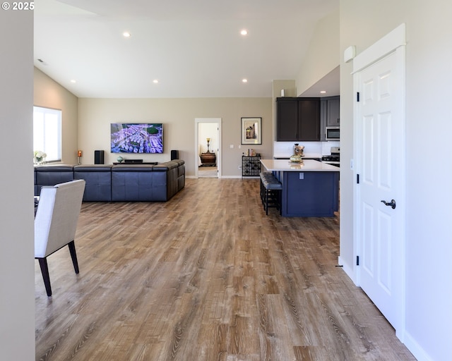 interior space with a breakfast bar area, wood finished floors, lofted ceiling, light countertops, and open floor plan