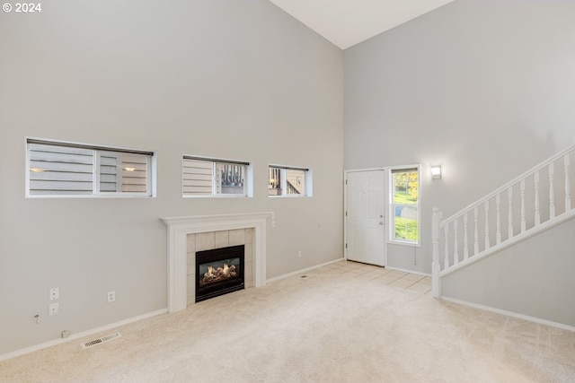 unfurnished living room with high vaulted ceiling, light colored carpet, and a tile fireplace