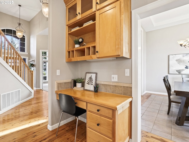 office space featuring light wood-type flooring, built in desk, and a notable chandelier