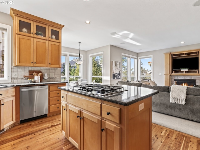 kitchen featuring appliances with stainless steel finishes, a kitchen island, decorative light fixtures, dark stone counters, and light wood-type flooring