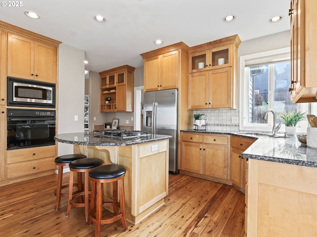 kitchen with sink, light wood-type flooring, dark stone counters, a center island, and stainless steel appliances