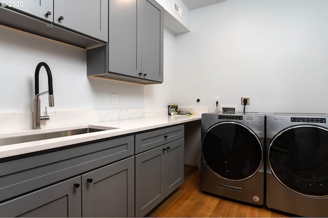 laundry room with cabinets, light hardwood / wood-style floors, washer and dryer, and sink