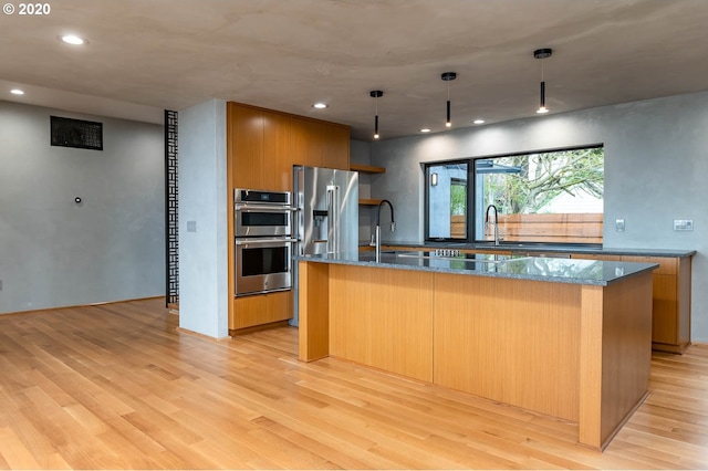 kitchen with a kitchen island with sink, light hardwood / wood-style flooring, hanging light fixtures, and appliances with stainless steel finishes