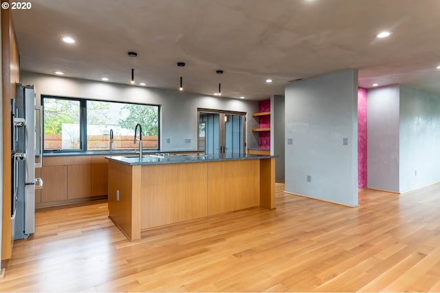 kitchen with light wood-type flooring, sink, a large island with sink, dark stone countertops, and oven