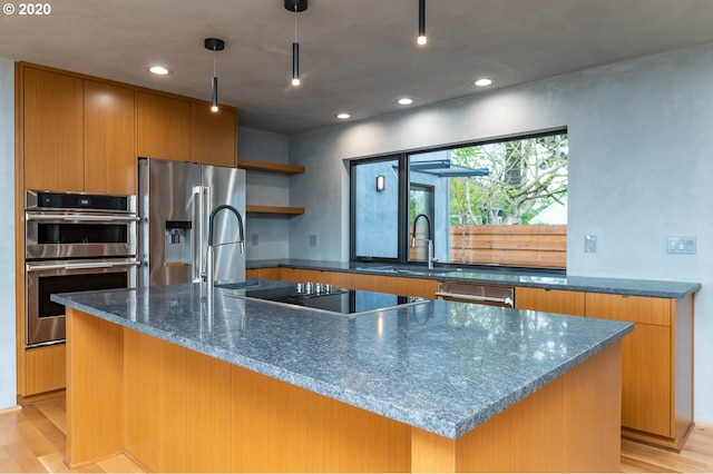 kitchen with light wood-type flooring, stainless steel appliances, and an island with sink