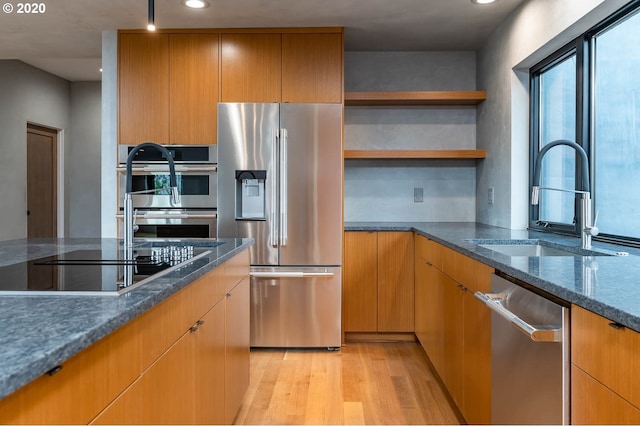 kitchen featuring light wood-type flooring, stainless steel appliances, dark stone counters, and sink