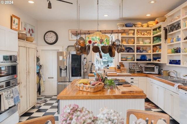 kitchen featuring sink, stainless steel appliances, tile floors, wood counters, and a center island