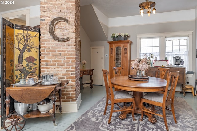 dining area with wood-type flooring, brick wall, and vaulted ceiling