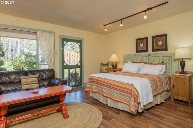 bedroom with wood-type flooring, track lighting, and access to outside