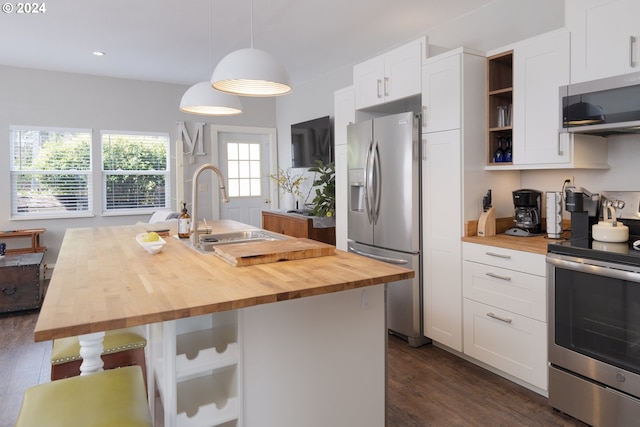 kitchen with pendant lighting, dark hardwood / wood-style flooring, appliances with stainless steel finishes, butcher block countertops, and a center island with sink