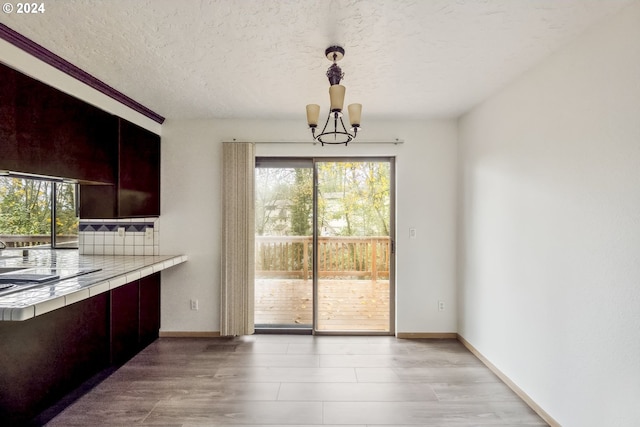 unfurnished dining area featuring a chandelier, a textured ceiling, and light hardwood / wood-style flooring