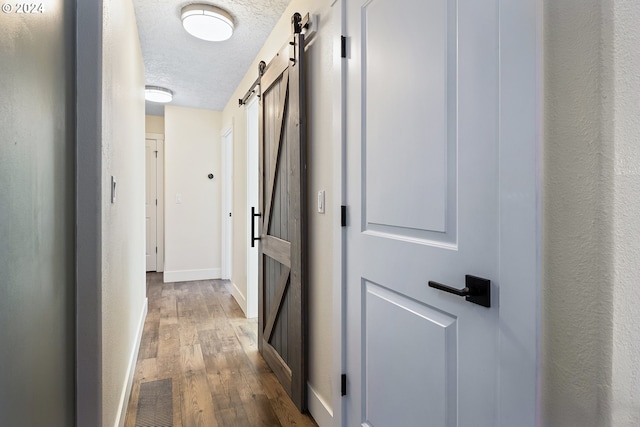 hallway featuring a textured ceiling, a barn door, and hardwood / wood-style flooring