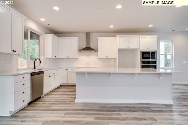 kitchen with white cabinets, stainless steel appliances, a center island, and wall chimney exhaust hood