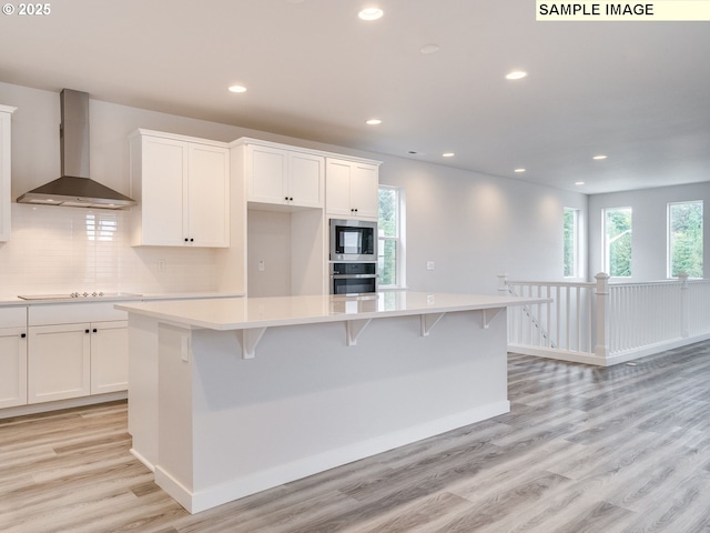 kitchen featuring light countertops, wall chimney range hood, appliances with stainless steel finishes, and white cabinetry