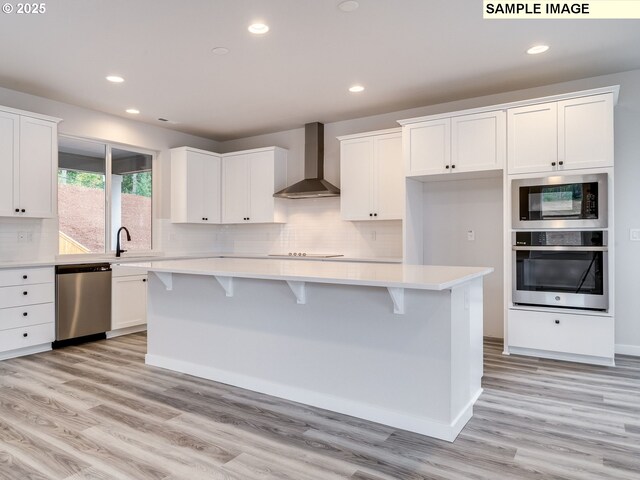 kitchen with stainless steel appliances, a kitchen island, white cabinetry, and wall chimney exhaust hood