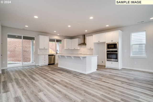 kitchen with white cabinets, appliances with stainless steel finishes, a kitchen island, and wall chimney range hood