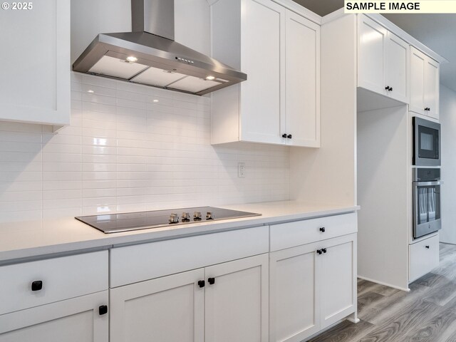 kitchen featuring white cabinets, a center island, wall chimney range hood, and appliances with stainless steel finishes