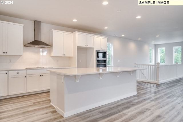 kitchen with a center island, wall chimney range hood, white cabinetry, and light hardwood / wood-style flooring