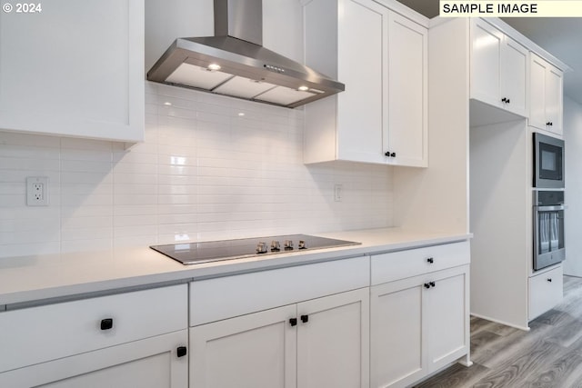 kitchen featuring built in microwave, wall chimney exhaust hood, white cabinetry, black electric stovetop, and oven