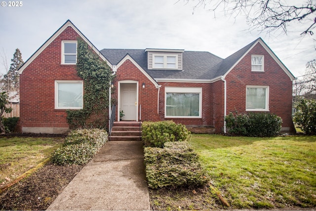 view of front facade featuring brick siding, a front yard, and a shingled roof