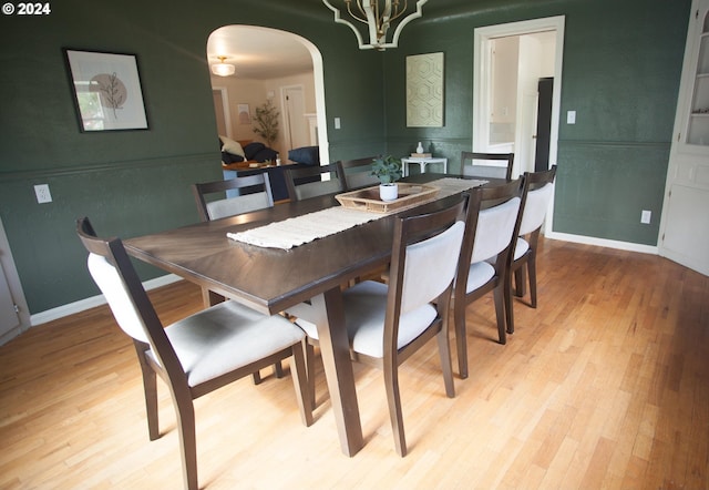 dining room featuring arched walkways, light wood-type flooring, a notable chandelier, and baseboards