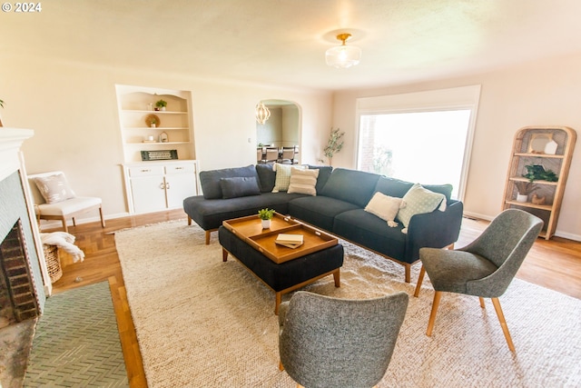 living room featuring baseboards, arched walkways, light wood-style flooring, built in shelves, and a fireplace