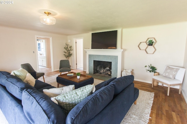 living area featuring a fireplace with flush hearth, dark wood-style flooring, and baseboards