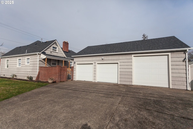 view of front of property featuring brick siding, a detached garage, a chimney, a shingled roof, and a front yard