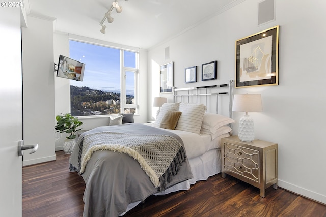 bedroom featuring dark hardwood / wood-style flooring, rail lighting, and crown molding