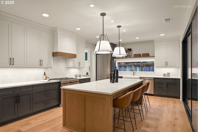 kitchen featuring white cabinetry, a center island, light hardwood / wood-style flooring, decorative light fixtures, and appliances with stainless steel finishes