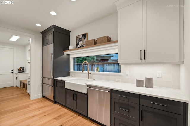 kitchen featuring backsplash, stainless steel dishwasher, sink, light hardwood / wood-style flooring, and white cabinets