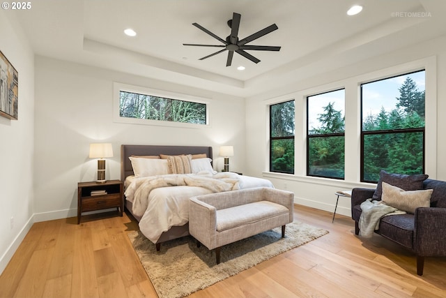 bedroom with ceiling fan, a raised ceiling, and light wood-type flooring