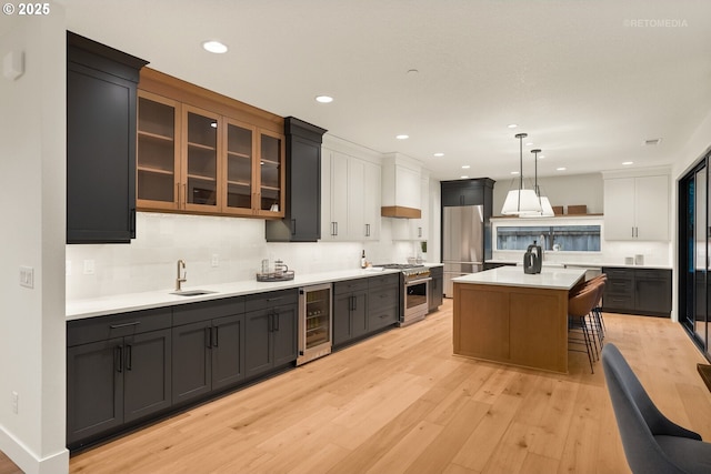 kitchen with hanging light fixtures, wine cooler, a kitchen bar, a kitchen island with sink, and appliances with stainless steel finishes