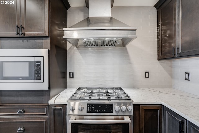 kitchen with backsplash, light stone countertops, wall chimney exhaust hood, appliances with stainless steel finishes, and dark brown cabinetry