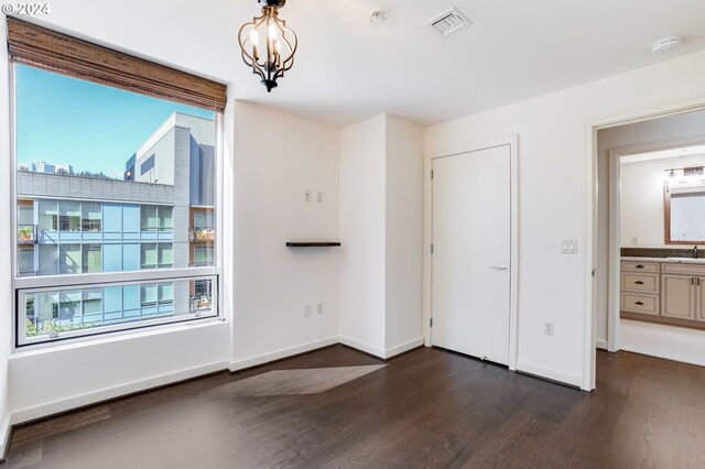 unfurnished bedroom featuring connected bathroom, sink, a chandelier, and dark hardwood / wood-style flooring