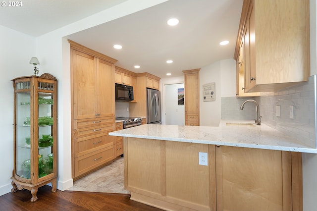 kitchen featuring appliances with stainless steel finishes, light stone countertops, a sink, a peninsula, and light brown cabinets