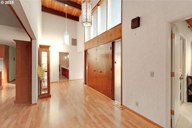 hallway with light wood-style floors, beam ceiling, visible vents, and wooden ceiling