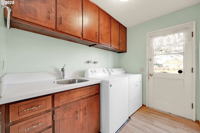 laundry room with independent washer and dryer, a sink, cabinet space, and light wood-style floors