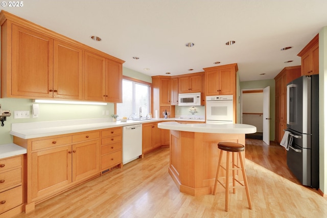 kitchen with white appliances, light wood finished floors, a kitchen island, a breakfast bar area, and a sink