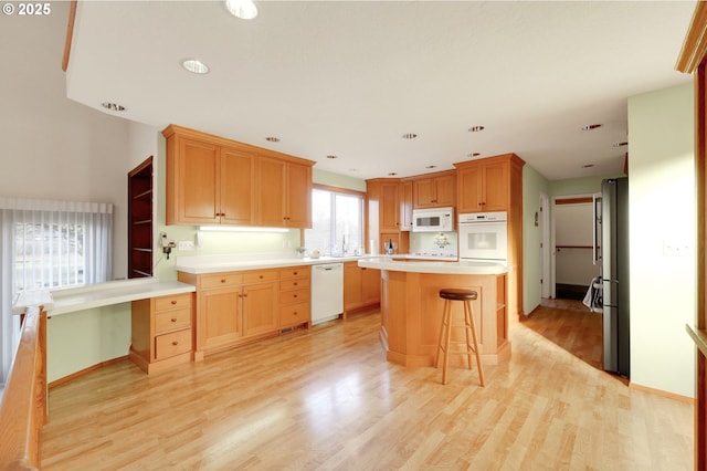 kitchen with light countertops, light wood-style floors, a kitchen island, white appliances, and a kitchen bar