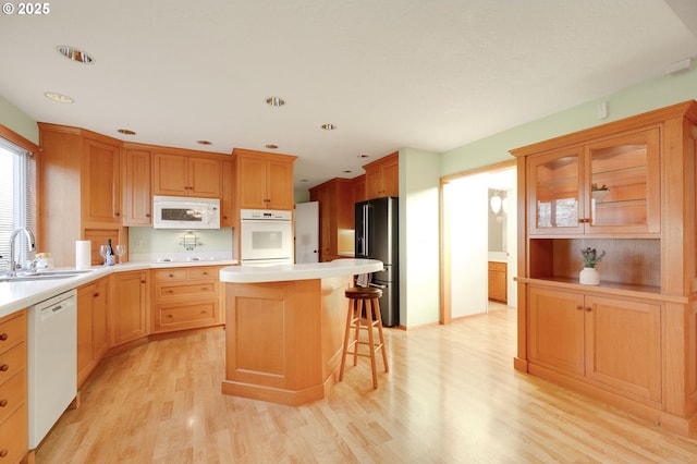 kitchen featuring a breakfast bar area, white appliances, a sink, light countertops, and light wood-type flooring