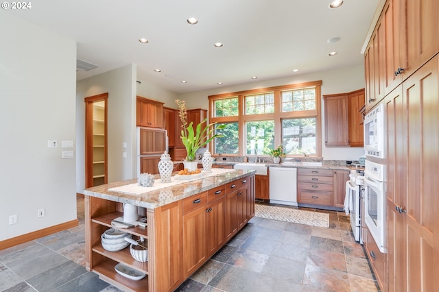 kitchen with light stone counters, built in appliances, sink, and a center island