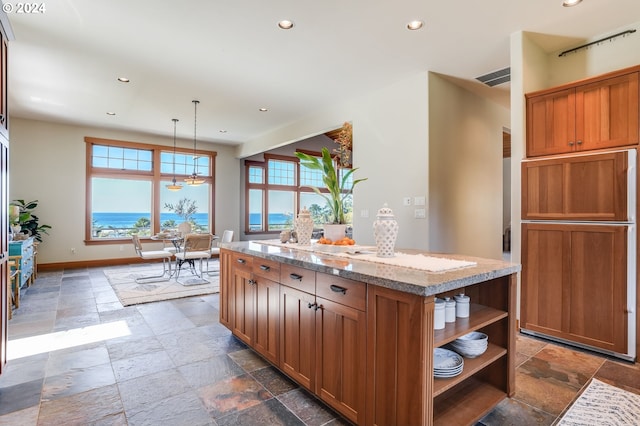 kitchen with a water view, a center island, light stone countertops, and decorative light fixtures