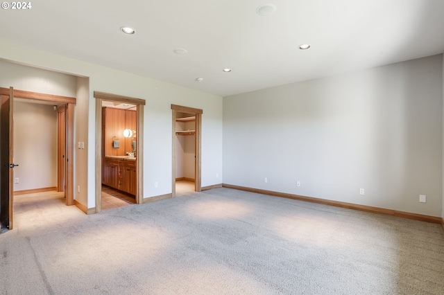 unfurnished bedroom with light carpet, connected bathroom, and a spacious closet