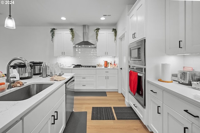 kitchen with stainless steel appliances, sink, wall chimney range hood, light hardwood / wood-style flooring, and white cabinets