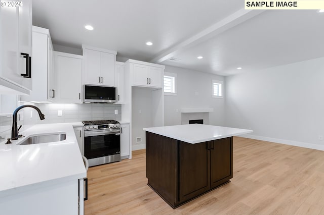 kitchen featuring beam ceiling, sink, stainless steel appliances, a kitchen island, and light wood-type flooring