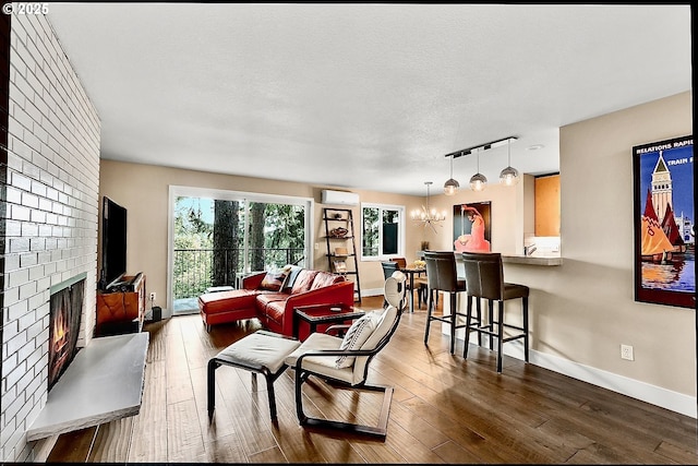 living room with an inviting chandelier, a wall mounted air conditioner, a fireplace, wood-type flooring, and a textured ceiling